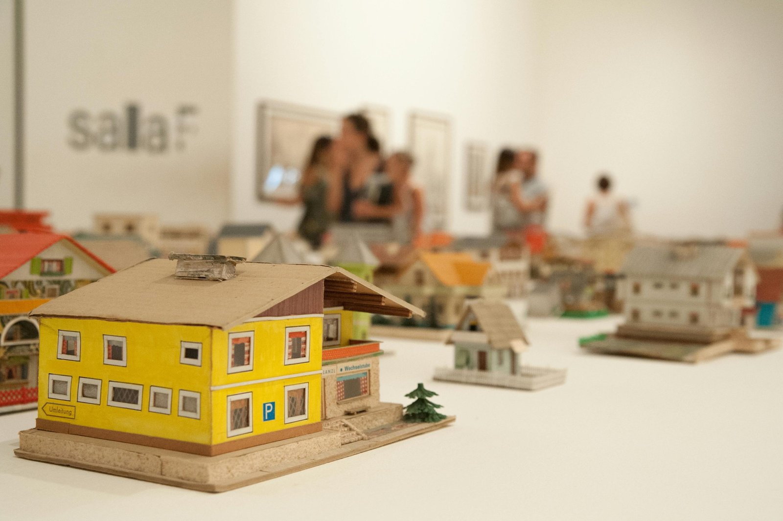 Detailed miniature house models displayed in an indoor exhibition setting with people in the background.