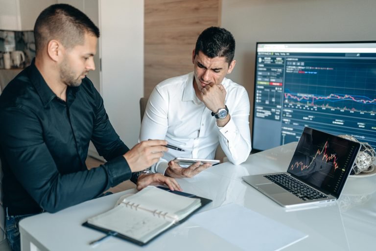 Two men discussing business analytics in an office with laptops and graphs.