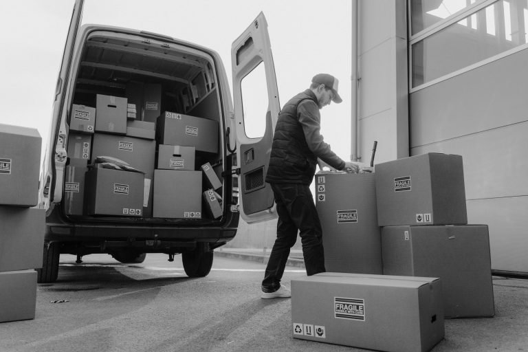 Delivery driver unloads packages from a van, organizing shipments outdoors.