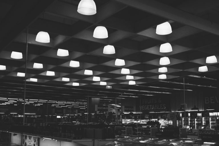 A black and white interior view of a modern supermarket with hanging lights.
