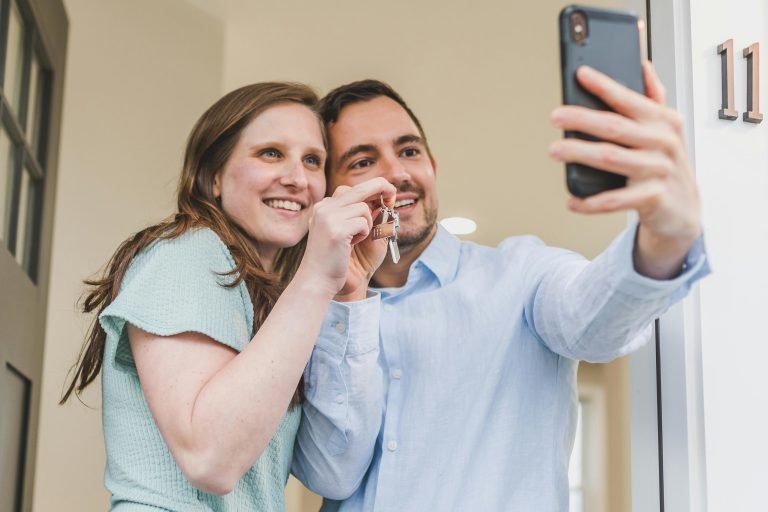 Joyful couple taking a selfie while holding keys to their new home, celebrating a milestone.