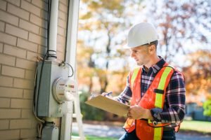 A man in an orange vest and hard hat inspects a meter, promoting home safety inspections by electricians near Germantown, TN.