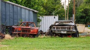 A collection of old cars parked in a yard, showcasing various models and conditions, possibly for a junk car service.