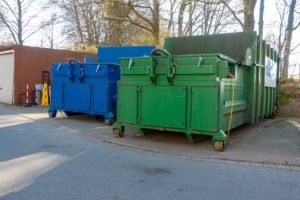 Two green roll-off dumpsters positioned side by side on a concrete surface.