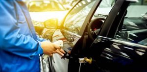 A man in blue overalls holds a cell phone, representing a locksmith service for replacing car keys.