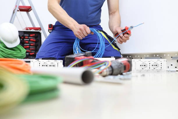 A man on a ladder is focused on electrical work in a room, weighing the decision to rewire his house himself.
