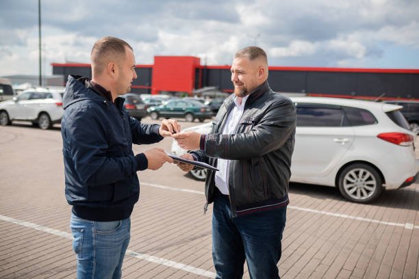 Two men are engaged in conversation next to a local used car and truck, sharing insights about the vehicle.