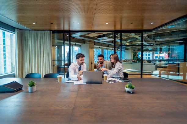 Three individuals seated at a conference table, each using a laptop, engaged in a discussion about mortgage lending.