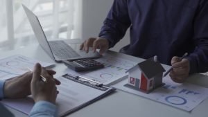 Two individuals at a table with a laptop and documents, discussing a loan for land and home construction in Herriman, UT.