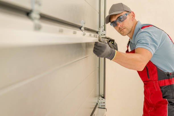Two men wearing overalls and hard hats actively working on installing a garage door in a residential garage.
