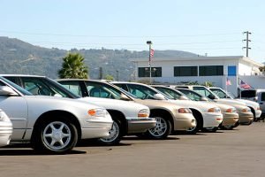 A row of used cars and trucks parked neatly in a parking lot under clear skies.