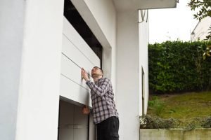A man stands in front of a closed garage door, appearing to troubleshoot a malfunctioning garage door opener.
