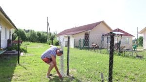 A man installs a chain-link fence in a yard, focused on his work in Cary, NC.
