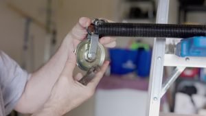 A man repairs a garage door opener, focusing on the garage door spring mechanism.