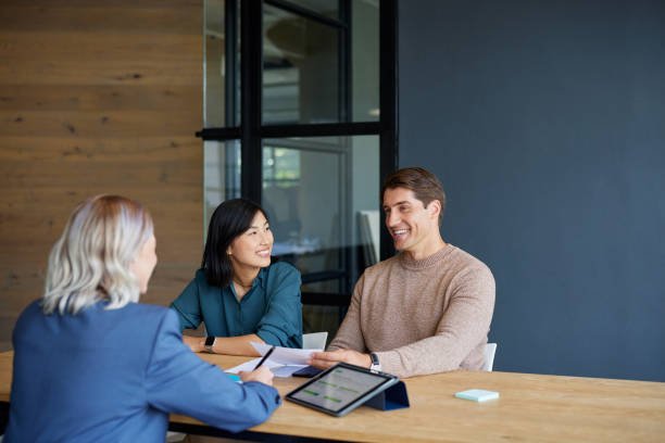 A mortgage broker and a client sit at a table, examining various papers related to mortgage options.