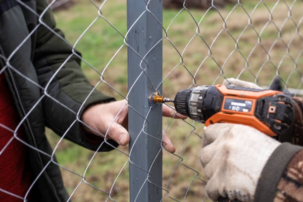 A man is engaged in installing a chain-link fence in a yard in Cary, NC.