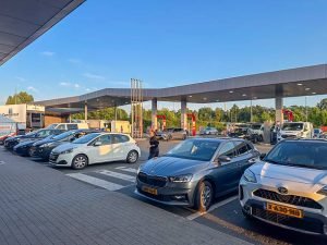 Cars parked at Motors Trust Dealer gas station in Los Lunas, NM, under bright sunlight.