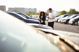 A man and woman stand in front of parked cars, representing car dealers assisting buyers with various credit situations.