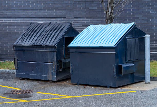 Two front-load dumpsters parked side by side on a concrete surface.