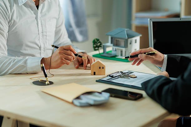  A woman's hand writes on paper with a pen, accompanied by a house model, symbolizing mortgage broker services in Gastonia, NC.