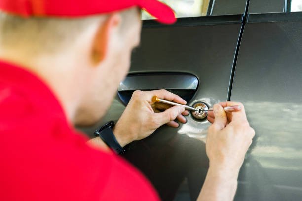 A man wearing a red shirt is fixing a car door handle, representing automotive locksmith services near Oil City for car keys.