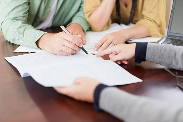  A woman's hand writes on paper with a pen, next to a small house model, illustrating mortgage guidance for homebuyers.
