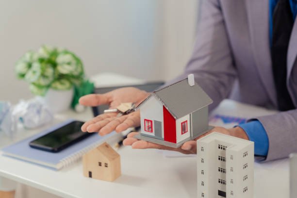 A woman's hand holds a pen, writing on paper beside a house model, symbolizing mortgage guidance for homebuyers.
