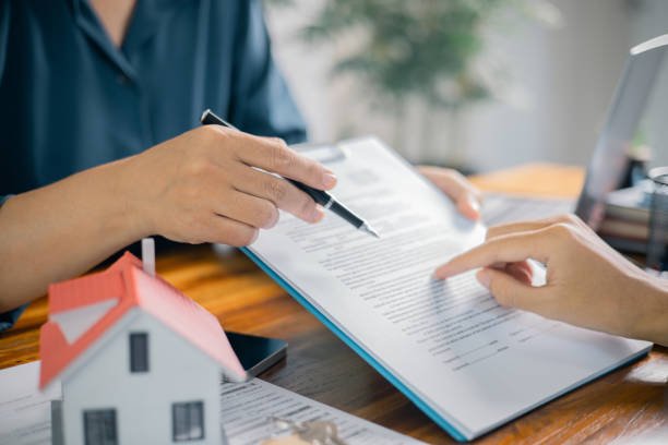 A woman's hand holds a pen, writing on paper beside a house model, symbolizing mortgage guidance for homebuyers.