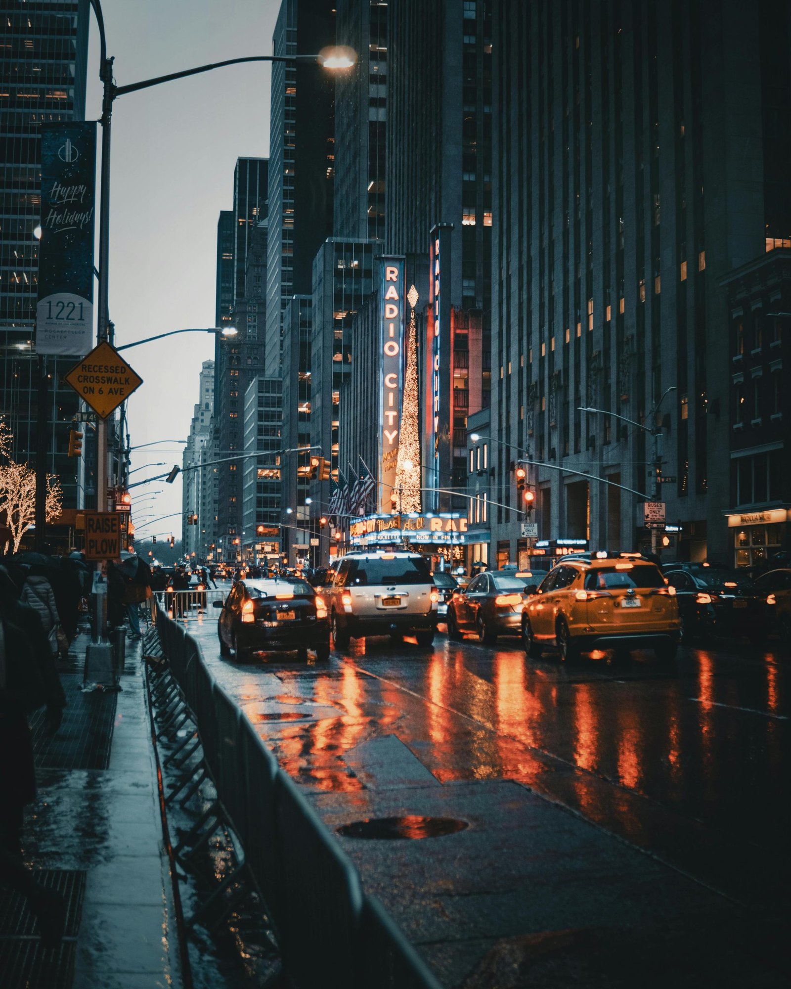 Dramatic city street view of New York's Radio City at night with reflections and taxis.