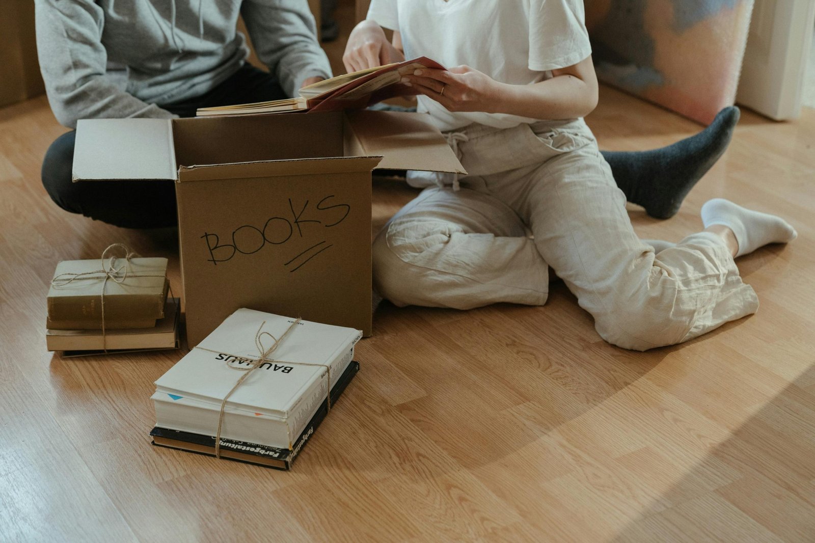 A couple sitting on the floor, unpacking books from cardboard boxes in their new apartment.