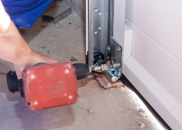 A man in overalls and a hard hat repairs a garage door, focusing on installation and maintenance tasks.
