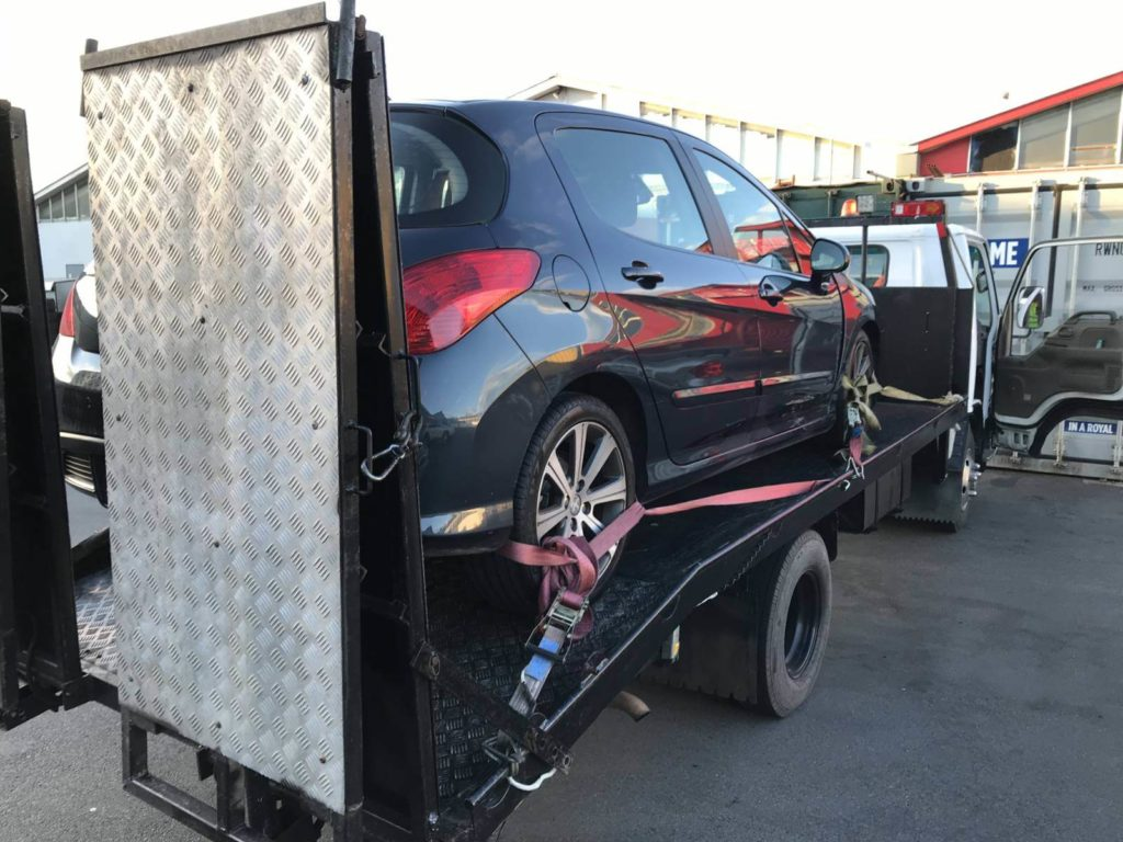 A tow truck stationed by the road, featuring a sign that reads "Instant Cash For Cars."