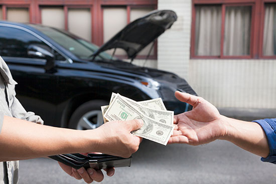 A man hands a car key to a woman, who holds a stack of cash, symbolizing a car sale transaction.