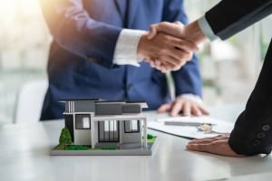 Two businessmen shaking hands over a house model, signifying a successful agreement with a trusted mortgage lender.