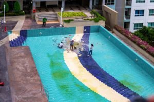 A man in a blue shirt is maintaining a blue swimming pool, highlighting the services of Lily Pads Pools & Ponds in Krum, TX.