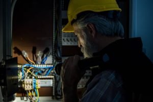An older man in a hard hat reviews an electrical panel during an Emergency Master Electrician Inspection in Lakeland, TN.