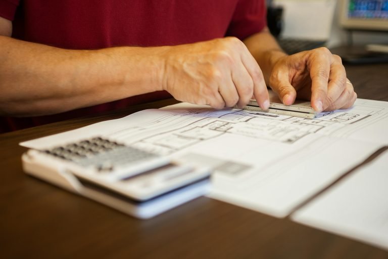 Close-up of an architect using a ruler to examine blueprints on a desk.
