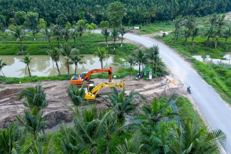 Aerial shot of excavators working on a construction site surrounded by palm trees and greenery.