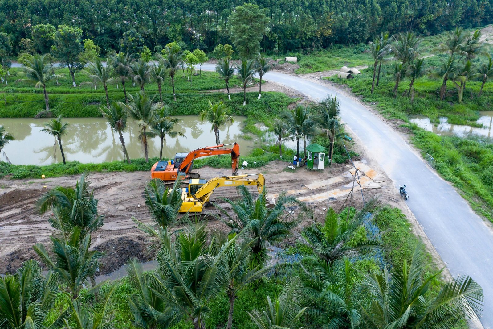 Aerial shot of excavators working on a construction site surrounded by palm trees and greenery.