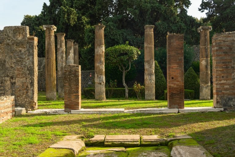 Historic columns in Pompeii with garden backdrop, ancient architecture focus.