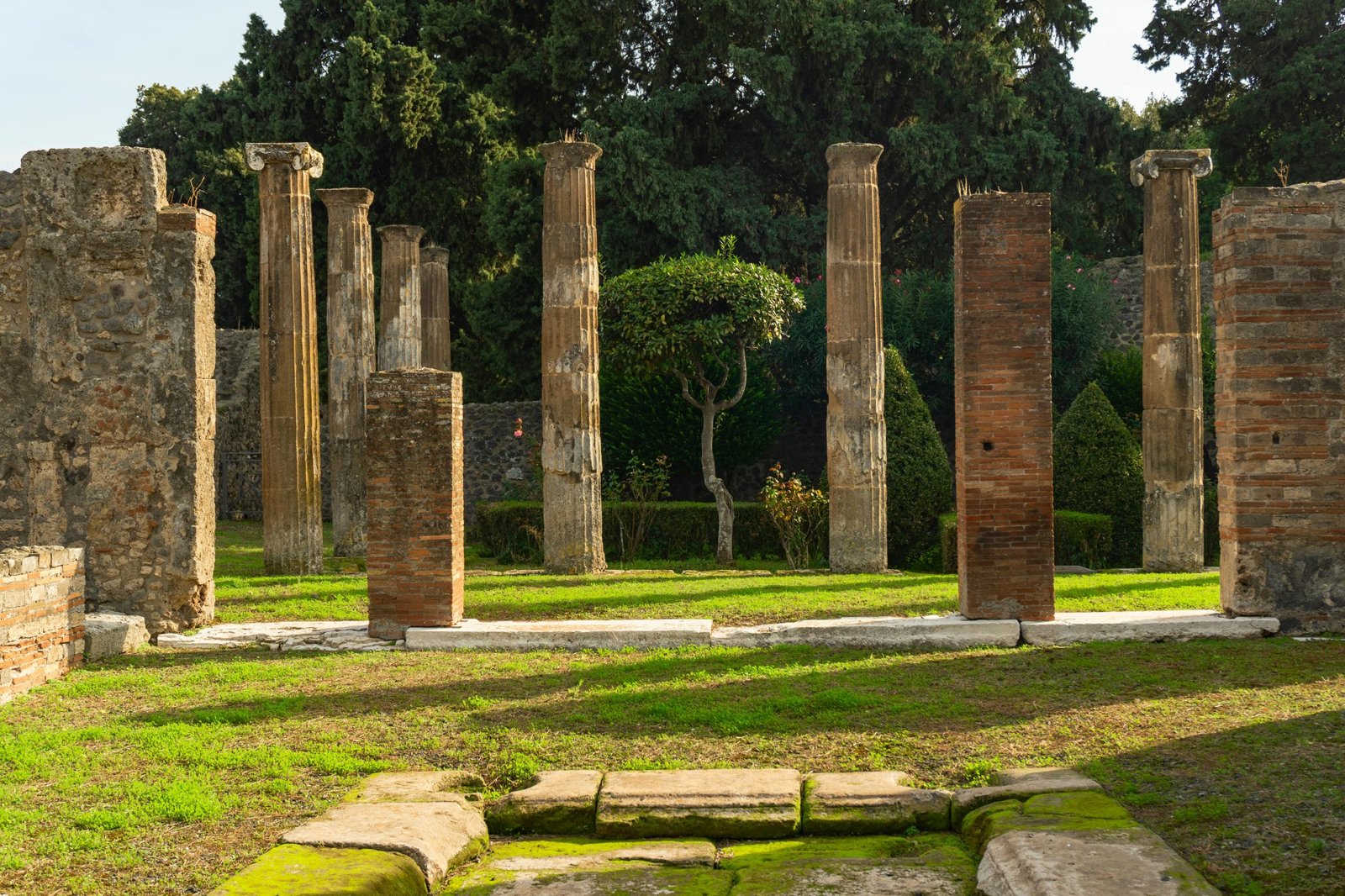 Historic columns in Pompeii with garden backdrop, ancient architecture focus.