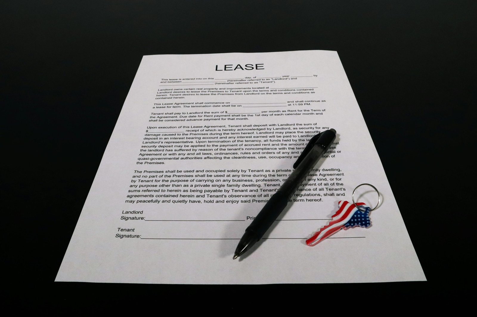 Lease agreement document with pen and American flag keychain on a black table.