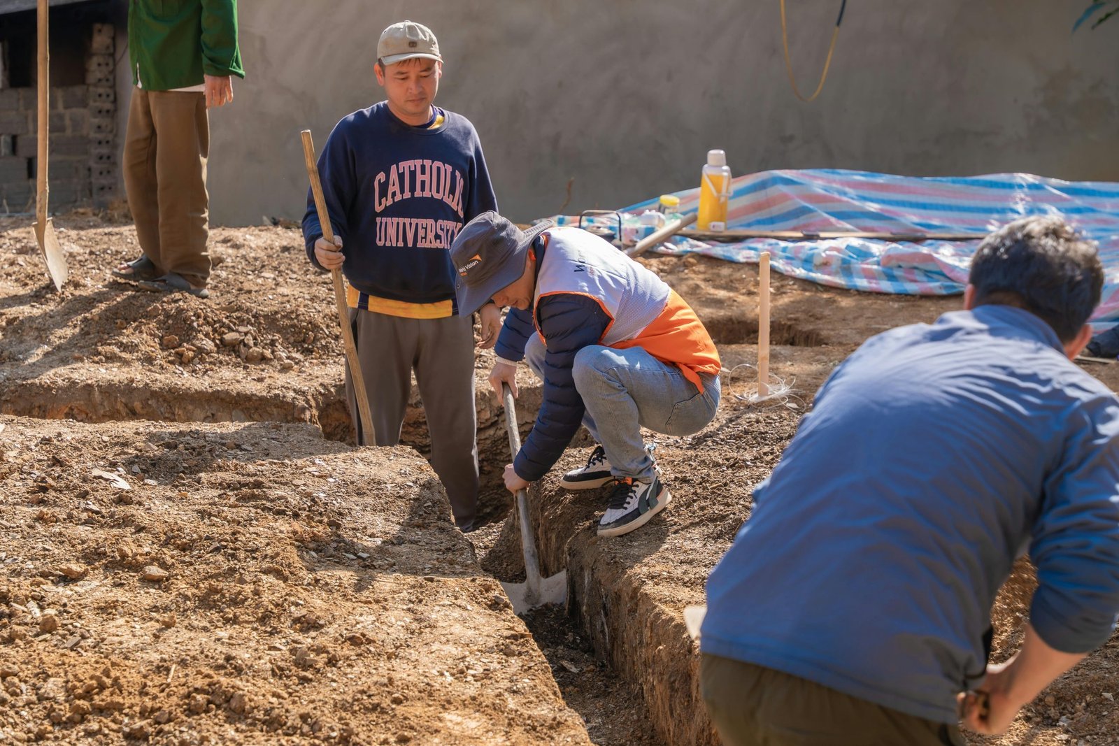 A group of four adult men working on a construction site digging a trench.
