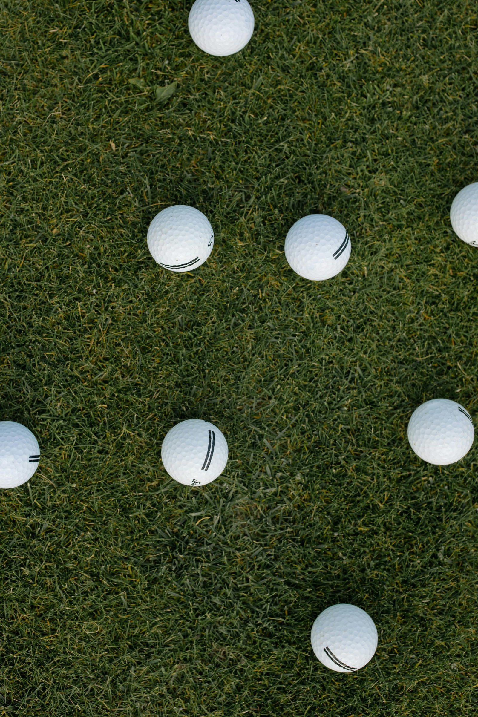 Scattered golf balls on lush green grass viewed from above, offering an ideal sports background.