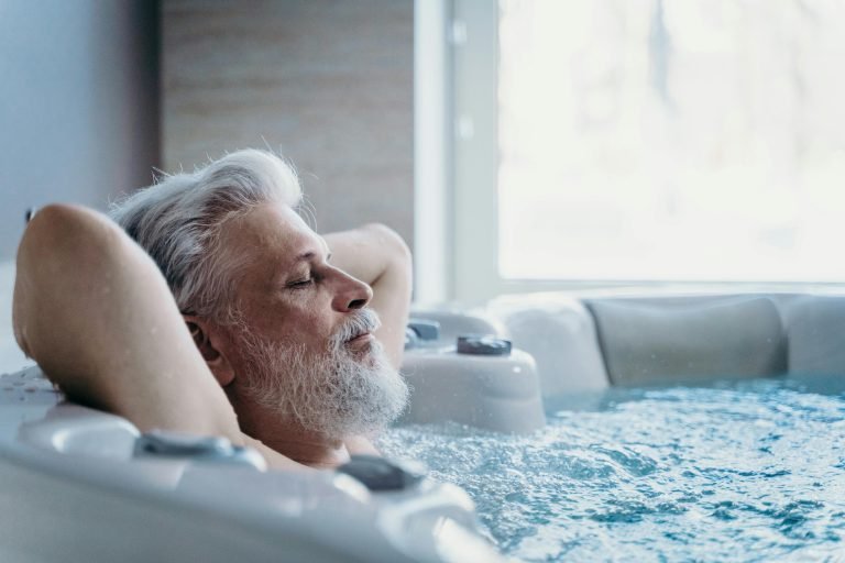 Elderly man with grey hair enjoys relaxation in an indoor jacuzzi, symbolizing wellness and leisure.