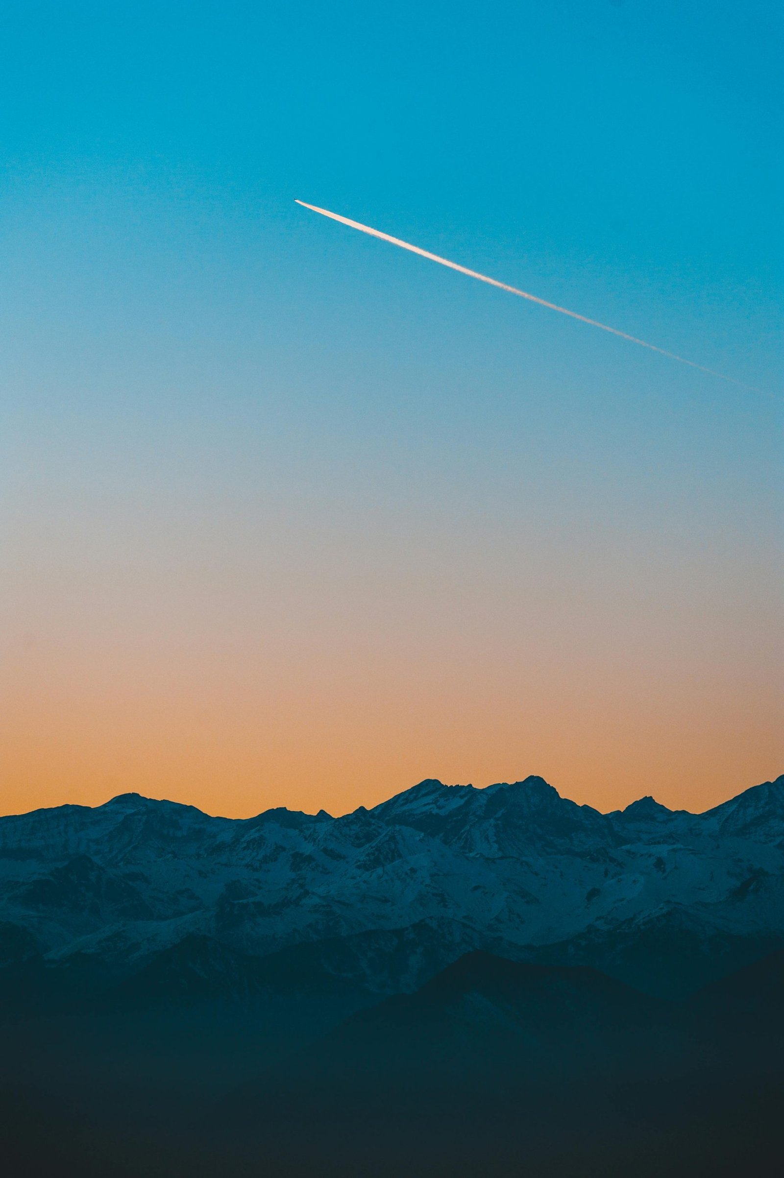 Scenic mountain view at sunset with a contrail streaking across the sky.