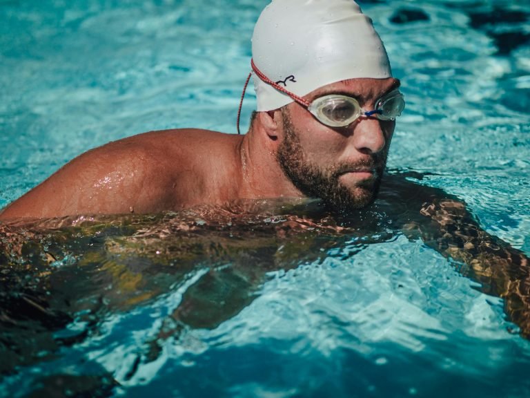 Male swimmer with white cap and goggles focused during swim in pool.