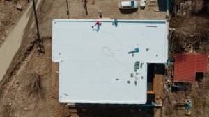 Top-down view of a house with workers on the roof, highlighting flat roofing work in Bergen County, NJ.
