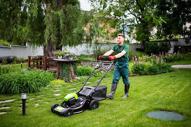 A man in green overalls is mowing grass, illustrating professional landscaping services offered in Gainesville.