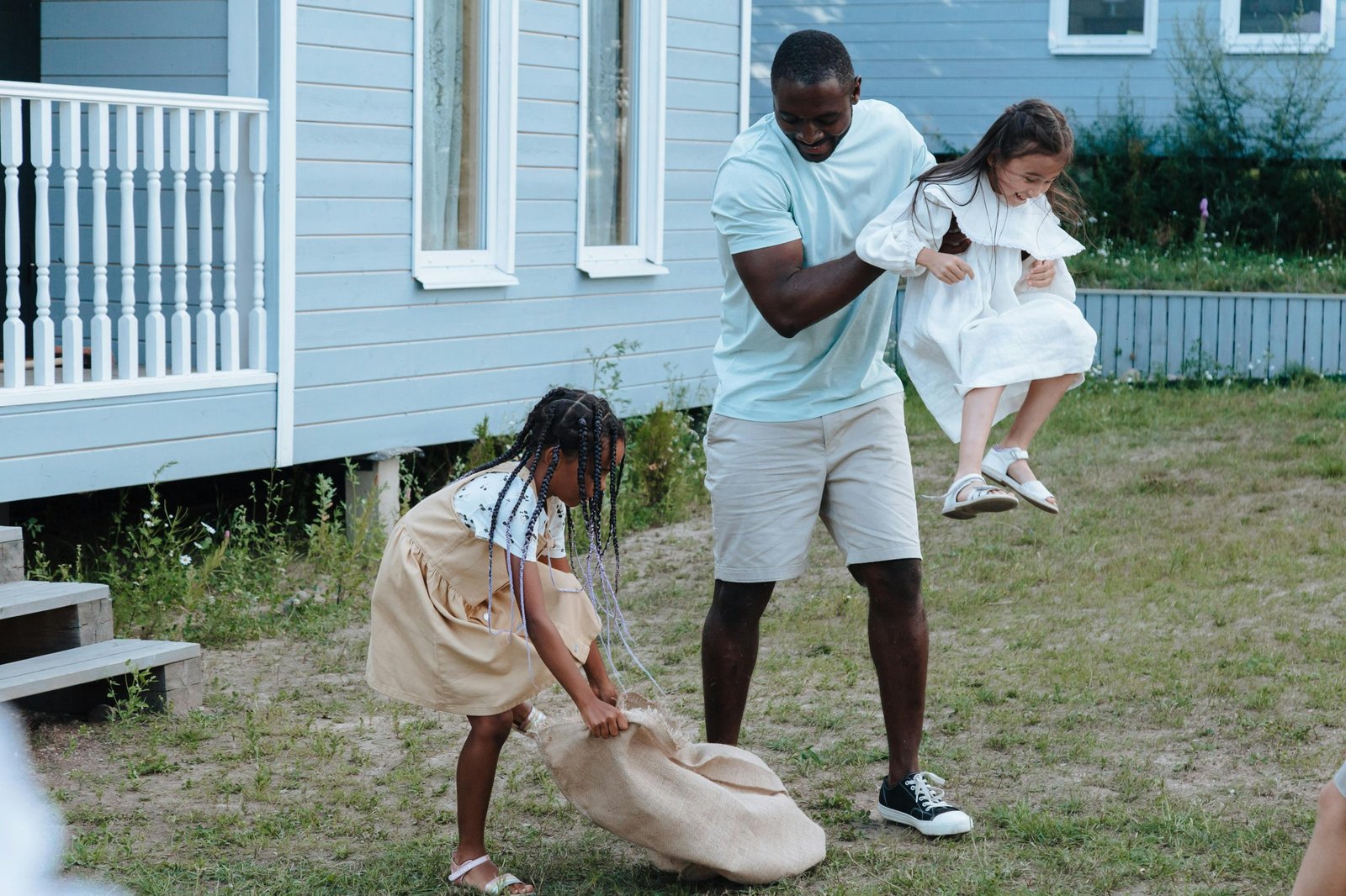 Father and daughters enjoying a playful day outdoors in the yard with smiles and laughter.